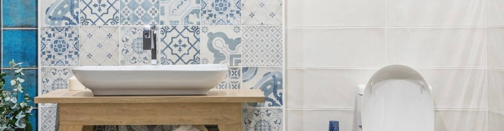   Banheiro com azulejos brancos e azuis, com espelho, pia retangular em cima de bancada de madeira, privada e itens de decoração azuis e brancos.