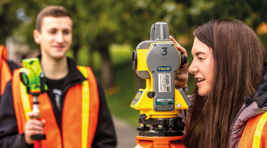 Homem e mulher topógrafos analisando equipamento.