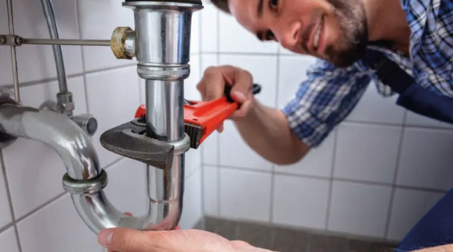 Encanador realizando a instalação de esgoto em uma pia de cozinha.